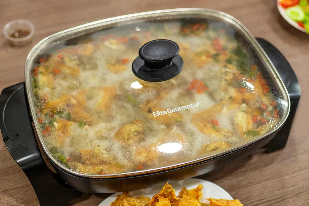 Elite Gourmet Electric Skillet EG-6203 is cooking up a chicken hot pot with different vegetables and pieces of chicken.