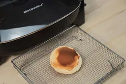 The bottom side of a golden brown pancake inside an air fryer basket. In the corner is the Elite Gourmet Non-Stick Electric Skillet EG-6203.