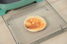 The bottom side of a golden brown pancake that’s dark around the edges inside an air fryer basket. In the corner is the GreenLife Ceramic Non-Stick Electric Skillet