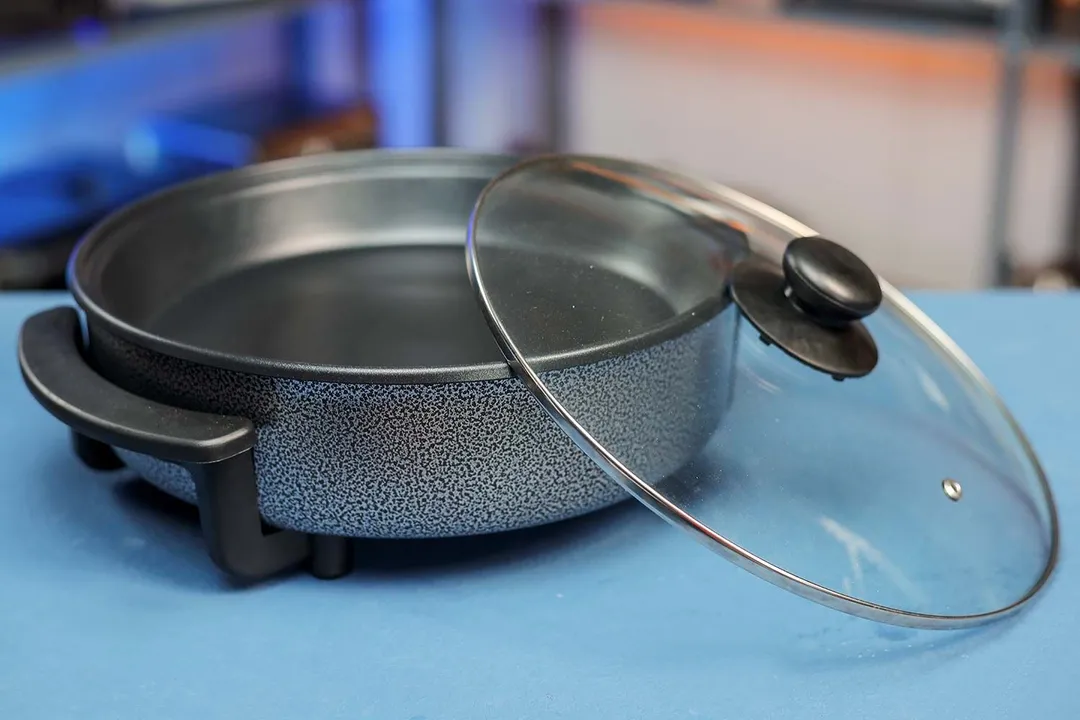 The Ovente Electric Skillet SK11112B with its lid leaning onto the rim.