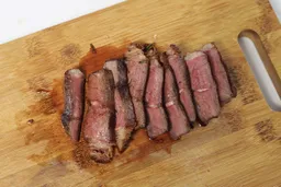 Slices of medium-rare steak on a wooden cutting board.