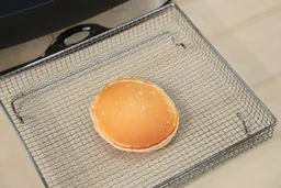 The top side of a golden brown pancake inside an air fryer basket. In the corner is the Presto Foldaway Non-Stick Electric Skillet 06857.