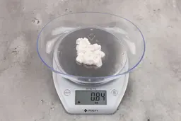 0.84 ounces of ground chicken scraps from garbage disposal, displayed on digital scale, placed on granite-looking table. Mess of shredded soft tissue and few pieces of shredded bones.