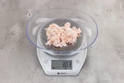 3.03 ounces of ground chicken scraps from garbage disposal, displayed on digital scale, placed on granite-looking table. Mess of shredded soft tissue and pieces of shredded bones.