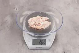 2.02 ounces of fibrous soft tissue and pieces of shredded bones, on digital scale, on granite-looking table.