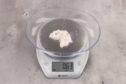 0.63 ounces of shredded soft tissue and few pieces of shredded bones, on digital scale, on granite-looking table.