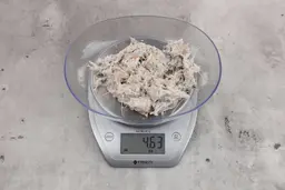 4.63 ounces of visible fish pin bones among mess of raw fibrous tissue on digital scale, on granite-looking table.