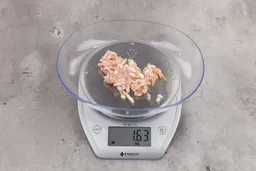 1.63 ounces of crushed chicken bone and cartilage, and shredded tendon and meat on digital scale on granite-looking top.