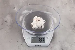 1.37 ounces of shredded fatty tissue and broken cartilage from chicken scraps on digital scale on granite-looking top.