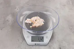 1.12 ounces of crushed chicken bone, shredded tendon, and fatty tissue on digital scale on granite-looking top.