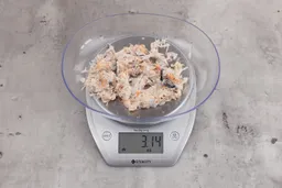  3.14 ounces of visible pin bones in a mass of raw meat and skin from fish scraps on digital scale on granite-looking top.