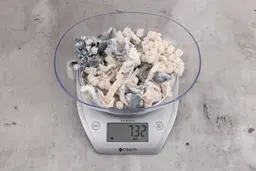 7.32 ounces of broken fish vertebrae and shredded fish skin on digital scale on granite-looking top.