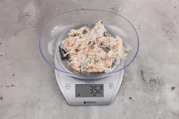 3.52 ounces of visible pin bones in a mass of raw meat and skin from fish scraps on digital scale on granite-looking top.