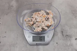 3.01 ounces of ground fish scraps from garbage disposal, displayed on digital scale, placed on granite-looking table. Mess of assorted shredded bones and raw fibrous tissue.