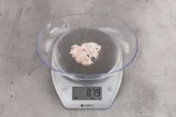 0.79 ounces of ground chicken scraps from garbage disposal, displayed on digital scale, placed on granite-looking table. Mess of shredded soft tissue and few pieces of shredded bones.