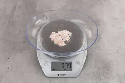 0.79 ounces of ground chicken scraps from garbage disposal, displayed on digital scale, placed on granite-looking table. Mess of shredded soft tissue and few pieces of shredded bones.