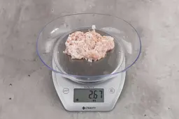 2.67 ounces of ground chicken scraps from garbage disposal, displayed on digital scale, placed on granite-looking table. Mess of fibrous soft tissue and pieces of shredded bones.