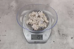 2.54 ounces of ground fish scraps from garbage disposal, displayed on digital scale, placed on a granite-looking table. Mess of assorted shredded bones and fibrous tissue.