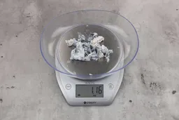 1.16 ounces of ground fish scraps from garbage disposal, displayed on digital scale, placed on granite-looking table. Fish vertebrae among mess of shredded fish skin.