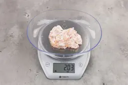 2.03 ounces of ground chicken scraps from garbage disposal, displayed on digital scale, placed on granite-looking table. Mess of shredded tendons and pieces of shredded bones.