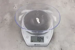0.04 ounces of ground chicken scraps from a garbage disposal, displayed on digital scale, placed on granite-looking table. Mess of soft tissue and pieces of shredded cartilage.
