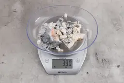 3.9 ounces of ground fish scraps from a garbage disposal, displayed on digital scale, placed on granite-looking table. Mess of shredded fish backbone and skin.