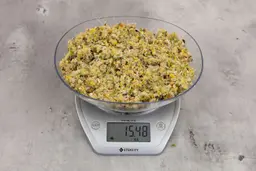 15.48 ounces of ground products from garbage disposal, displayed on digital scale, placed on granite-looking table. Mess of assorted scraps, including fibers, bones, etc.
