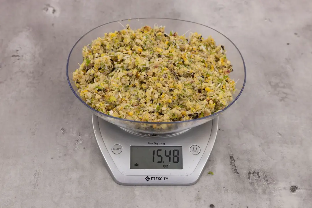 15.48 ounces of ground products from garbage disposal, displayed on digital scale, placed on granite-looking top. Visible fish pin bones in mess of assorted scraps, including dietary fiber, shredded bones, etc.