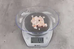 1.12 ounces of ground chicken scraps from garbage disposal, displayed on digital scale, placed on granite-looking table. Mess of shredded soft tissue and bones.