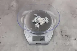 1.02 ounces of ground fish scraps from garbage disposal, displayed on digital scale, placed on granite-looking table. Fish vertebrae among mess of shredded fish skin.