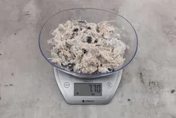 7.7 ounces of ground fish scraps from garbage disposal, displayed on digital scale, placed on granite-looking table. Visible pin bones among mess of raw fibrous tissue.