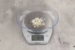 0.14 ounces of ground products from a garbage disposal, displayed on digital scale, placed on a granite-looking table. Shredded pieces of fish bones and vertebrae.