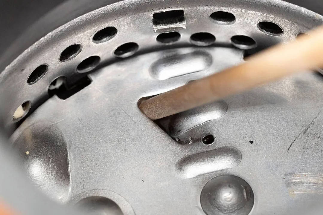 Inside view of garbage disposal showing manual unjam mechanics with wooden stick in flywheel’s opening/gap, partially showing details of flywheel and grater/grinder ring.