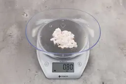 0.8 ounces of ground chicken scraps from garbage disposal, displayed on digital scale, placed on granite-looking table. Mess of shredded soft tissues and shredded bones.