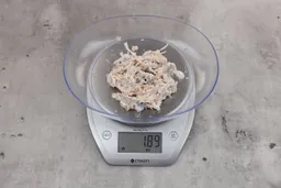 1.89 ounces of ground fish scraps from garbage disposal, displayed on digital scale, placed on granite-looking table. Mess of assorted shredded bones and raw fibrous tissue.