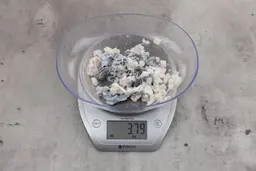 3.79 ounces of ground fish scraps from a garbage disposal, displayed on digital scale, placed on granite-looking table. Mess of shredded fish backbone and skin.
