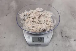 6.01 ounces of ground fish scraps from garbage disposal, displayed on digital scale, placed on granite-looking table. Pin bones among a mess of raw fibrous tissue.