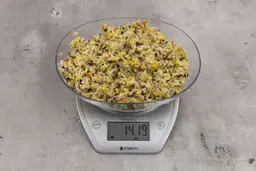 14.19 ounces of ground products from garbage disposal, displayed on digital scale, placed on granite-looking table. Mess of assorted scraps, including fibers, bones, etc.