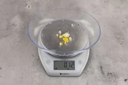 0.12 ounces of ground products from garbage disposal, displayed on digital scale, placed on granite-looking table. Shredded pieces of dietary fiber.