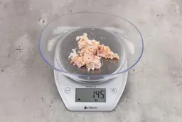 1.45 ounces of crushed chicken bone and cartilage, and shredded tendon and meat on digital scale on granite-looking top. 