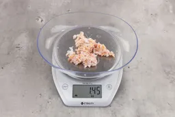 1.45 ounces of crushed chicken bone and cartilage, and shredded tendon and meat on digital scale on granite-looking top. 