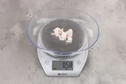 0.58 ounces of shredded fatty tissue and broken cartilage from chicken scraps on digital scale on granite-looking top.