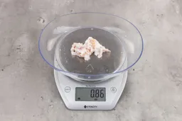 0.86 ounces of crushed chicken bone, shredded cartilage, and fatty tissues on digital scale on granite-looking top.