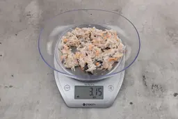 3.15 ounces of visible pin bones in a mass of raw meat and skin from fish scraps on digital scale on granite-looking top.