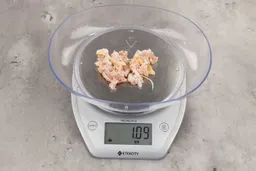 1.09 ounces of crushed chicken bone and cartilage, and shredded tendon and meat on digital scale on granite-looking top.