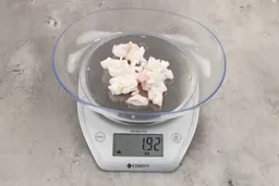 1.92 ounces of shredded fatty tissue and broken cartilage from chicken scraps on digital scale on granite-looking top.