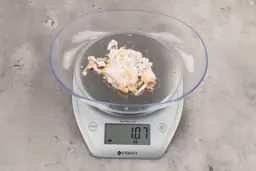 1.07 ounces of crushed chicken bone, shredded tendon, and fatty tissue on digital scale on granite-looking top.