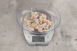 2.55 ounces of visible pin bones in a mass of raw meat and skin from fish scraps on digital scale on granite-looking top.