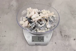 8.56 ounces of broken fish vertebrae and shredded fish skin on digital scale on granite-looking top.