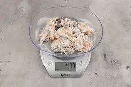 4.77 ounces of visible pin bones in a mass of raw meat and skin from fish scraps on digital scale on granite-looking top.